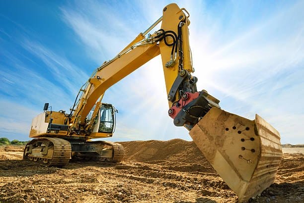 Big excavator on new construction site, in the background the blue sky and sun